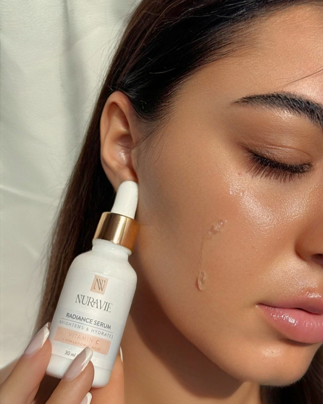 Woman applying Nuravie radiance serum to her face with a dropper.