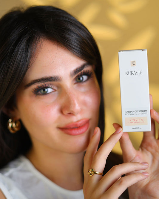 Woman holding a Nuravie radiance serum box against a blurred background