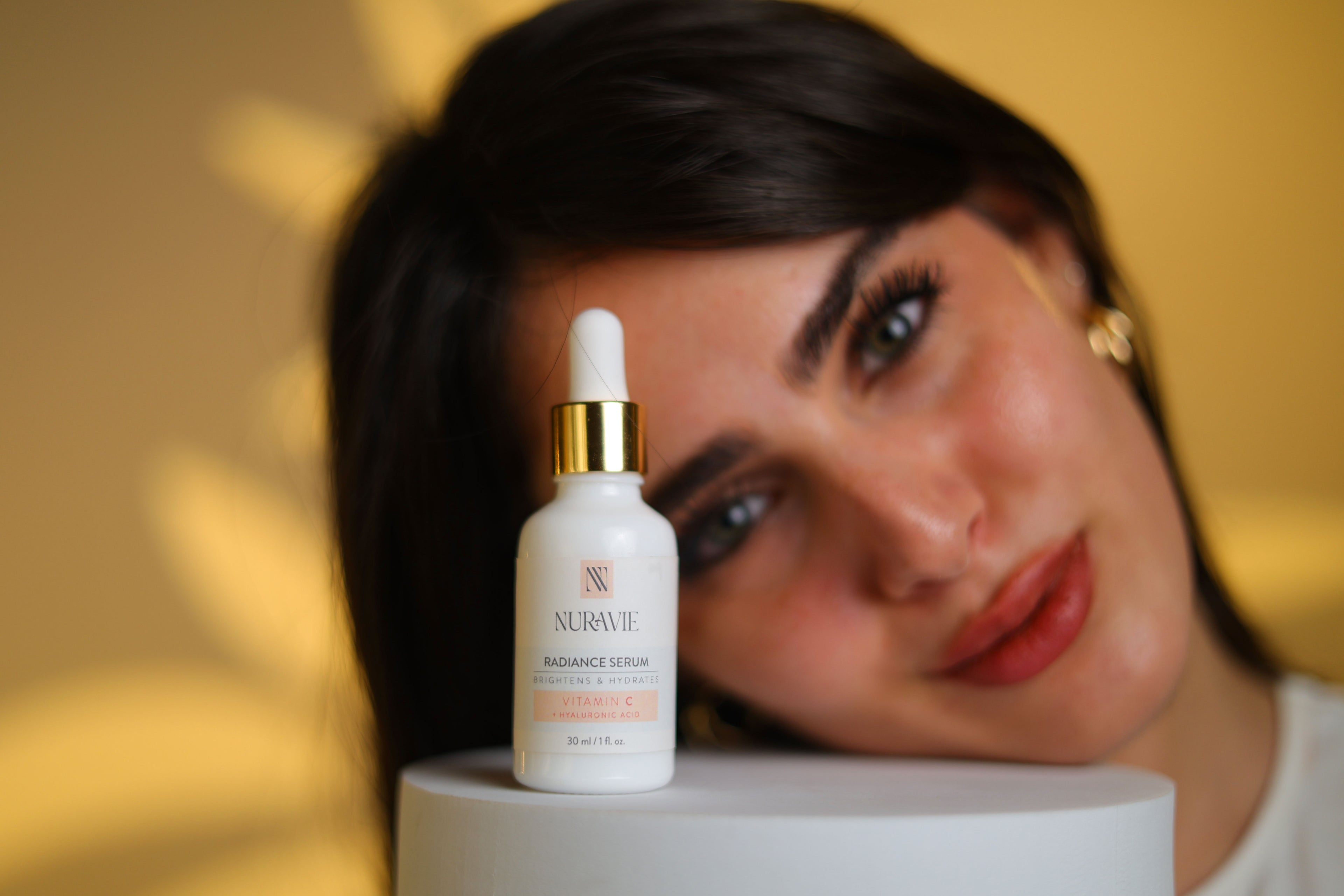 Woman with a bottle of Nuravie serum on a white surface with a blurred background
