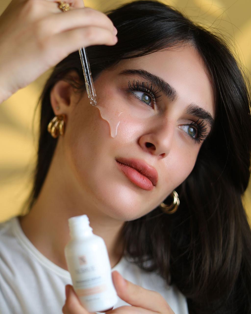 Woman applying a Nuravie Radiance serum with a dropper and bottle against a gold background